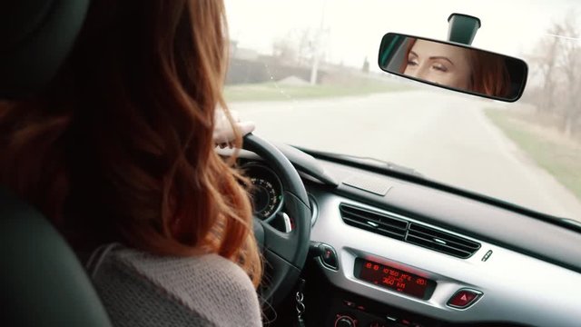 young red-haired woman driving car and looking in rear-view mirror