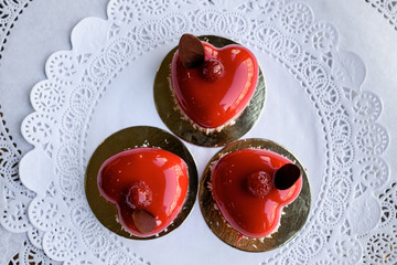 Three red cakes in form of hearts with raspberries on top