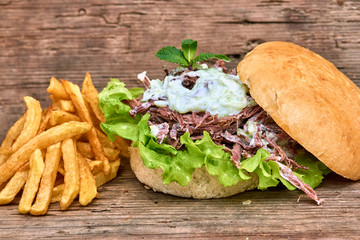 Barbeque Pulled Pork Sandwich with green salad,Tzatziki Sauce,BBQ Sauce and Fries on wooden background