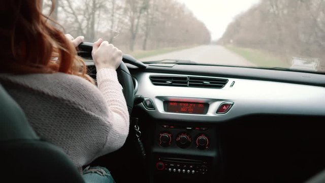 young red-haired woman rides in the car on the road, rear view
