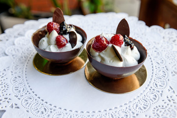 Two chocolate bowls with white cream and berries inside