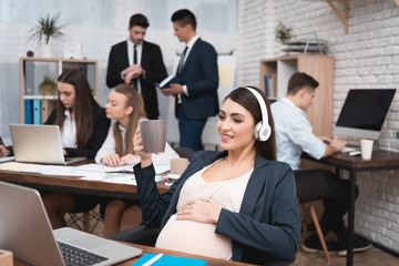 Beautiful pregnant woman listening to music with headphones in office.