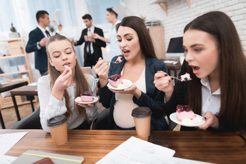 Three young girls eating sweet cake at lunchtime in office. Lunch break.