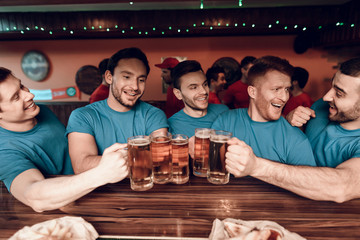 Blue team sports fans at bar drinking beer at sports bar with red team fans in background.