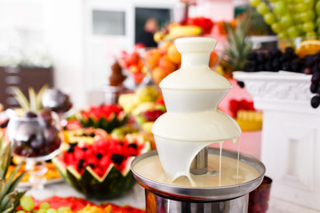 White Chocolate Fountain And Fruits For Dessert At Wedding Table
