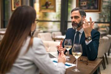 Business man sitting with his female colleague in a restaurant and talking about job while drinking...