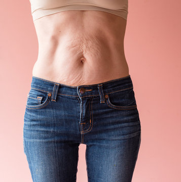 Midsection view of middle aged woman's bare natural looking stomach against peach pink background