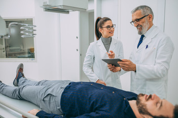 Mature doctor discussing with medical nurse while standing in hospital x ray machine room.