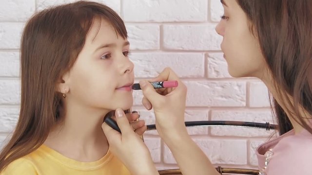 Do makeup to your child. The girl is put on lipstick lipstick.