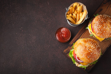 Tasty grilled home made burger with beef, tomato, cheese, cucumber and lettuce on a dark stone background with copy space. Top view. fast food and junk food concept