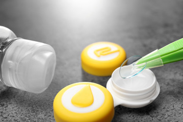 Taking contact lens from case on grey background, closeup