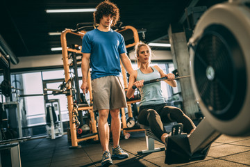 Young girl with her personal instructor in fitness center. Using rowing machine for cardio training in the gym.