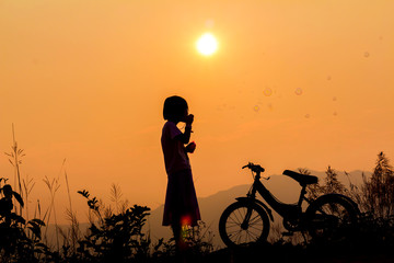 Obraz premium Silhouette little girl with bicycle playing with bubble wand on mountain at sunset background