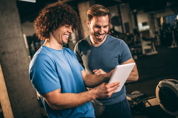 Fitness instructor showing training plan to his client in the gym. Happy young people at fitness center.