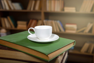 Сup of fresh coffee on a stack of old books in the library