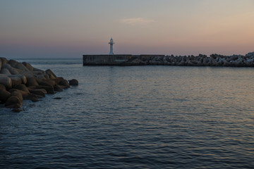 Fototapeta premium White lighthouse with purple light at a seawall with wavebreakers in Seogwipo, Jeju Island, South Korea