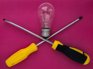 screwdrivers and a light bulb on a pink background