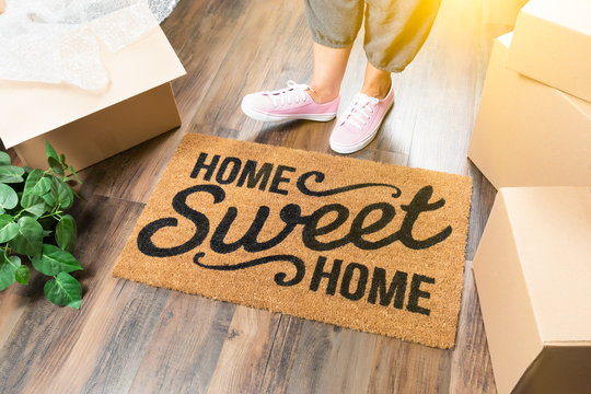 Woman in Pink Shoes and Sweats Standing Near Home Sweet Home Welcome Mat, Boxes and Plant