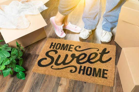 Man and Woman Standing Near Home Sweet Home Welcome Mat, Moving Boxes and Plant