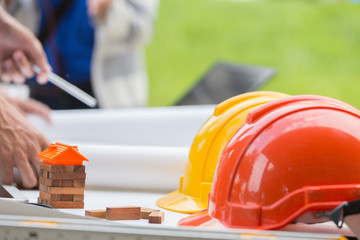 Engineer hard helment with house model and orange roof, working with tablet and computer and white plan