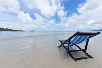 Blue wooden beach chair on the beach with white cloud and blue sky, as for summer season
