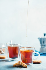 Morning coffee with cookies. Double wall glass cups with a Moka pot on a light concrete background. Pouring milk in coffee action food photography