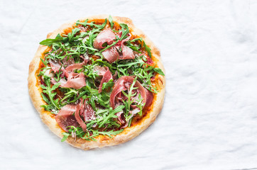 Prosciutto arugula homemade pizza on light background, top view. Delicious appetizers, snack, tapas in mediterranean style. Free space
