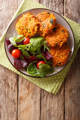 Homemade fritters of sweet potatoes and fresh mix of salad on a plate macro. Vertical top view