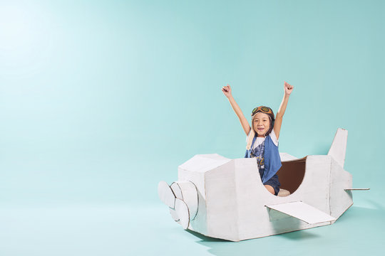 Little asian girl is happy sitting on a hand made cardboard paper plane . Isolated on mint green background .