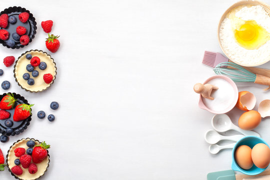 Baking utensils and cooking ingredients for tarts, cookies, dough and pastry. Flat lay with eggs, flour, sugar, berries.Top view, mockup for recipe, culinary classes, cooking blog.