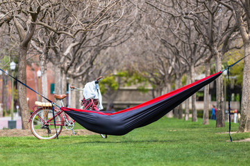 Obraz na płótnie Canvas Free spirit adventurous traveller taking break to relax and nap in hammock in city park