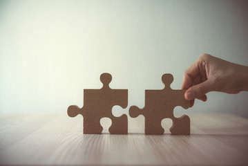 Closeup hand of woman connecting jigsaw puzzle on table wood, Business solutions, success and strategy concept