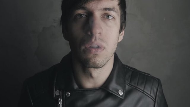 Brutal man in a leather jacket smokes a cigarette and drinks beer