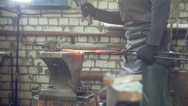 Muscular man blacksmith with hammer in forge creating steel knife