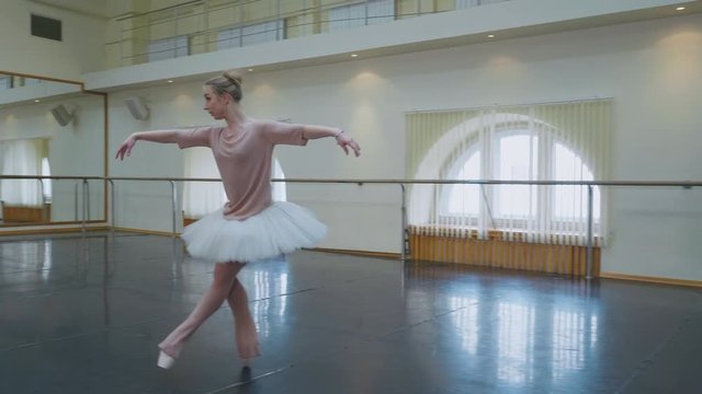 Ballerina in white ballet tutu dress practicing in dance studio or gym. Woman jumping in class room. Alone warming up before performance. Amazing dance. 4k