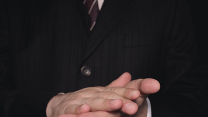 Businessman in suit, hands, black background.