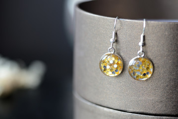 Resin earrings with yellow glitter on a dark background close up