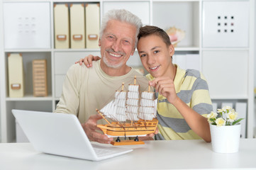 Boy and grandfather with a laptop and model of ship