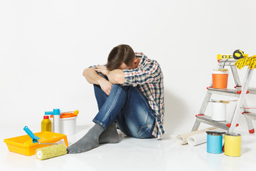 Confused shocked annoyed tired man sitting on floor with hands on head instruments for renovation apartment isolated on white background. Wallpaper, gluing accessories, tools. Repair home concept.