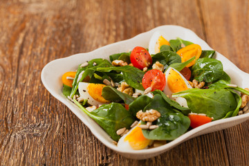 Delicious salad of fresh spinach, boiled egg, tomatoes, nuts and sunflower seeds