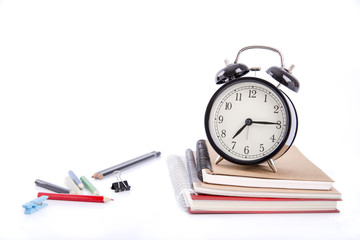 A pile of books and with coloured pen and alarm clock on white background