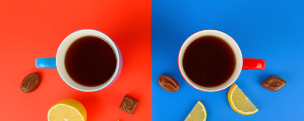 Red and blue cups with tea , lemon slices and chocolate candies on a red and blue background. Wide photo.
