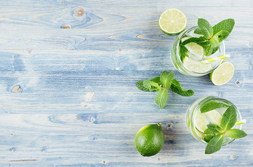Mojito in two glasses with mint, slices lime, ice cubes, straw on soft light blue background, copy...