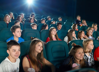 Schoolmates watching fancy cartoon in the cinema. Boys and girls looking happy,emotional, funny and satisfied. Children wearing colorful clothes with prints. Eating popcorn and drinking fizzy drinks.