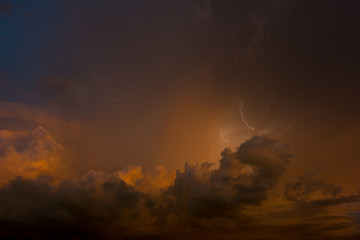 Stroke of lightning with storm clouds and golden sunset light
