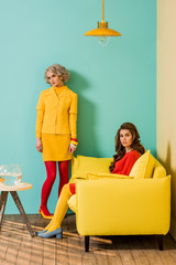 young retro styled women in colorful apartment with yellow sofa and aquarium fish, doll house...