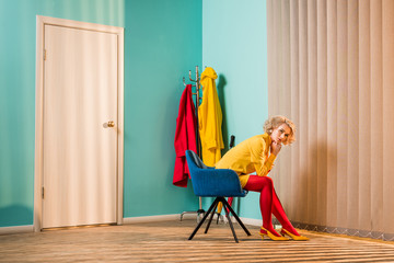 side view of retro styled woman sitting on chair at bright apartment, doll house concept