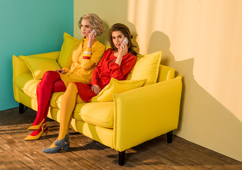retro styled women talking on smartphones on yellow sofa, doll house concept