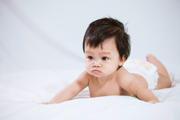 Cute asian baby girl wearing diaper lying on her stomach on the bed on white background