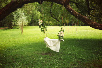 Elegant swings, decorated with flowers hanging from a tree branch in a glade in summer